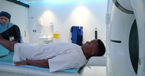 Male patient lying in ct scanner while female technician in headscarf operating console