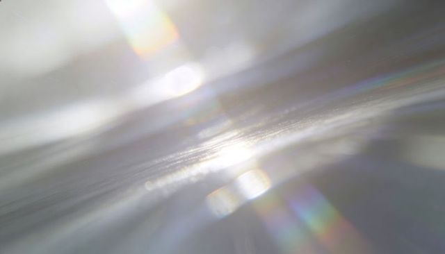 Iridescent prism light on textured surface creating shimmering abstract bokeh and flares