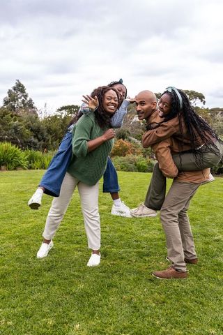 African american family giving piggyback rides in park, joyful outdoor family bonding