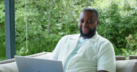 African man working remotely on laptop on garden patio, smiling and relaxed