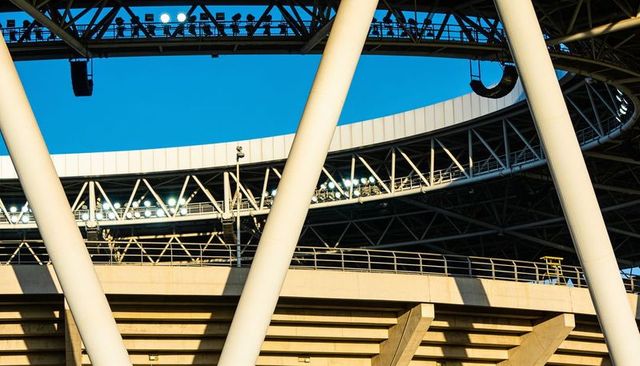Diagonal pylons framing stadium catwalk with floodlights and spectator silhouettes