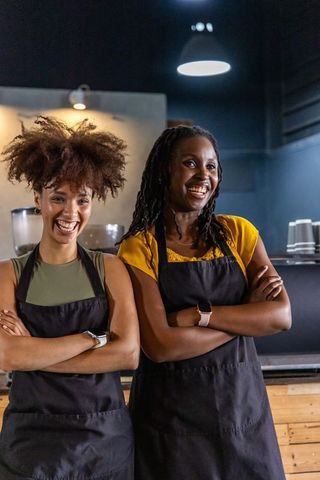 Confident african american baristas smiling and standing behind warm wooden coffee counter