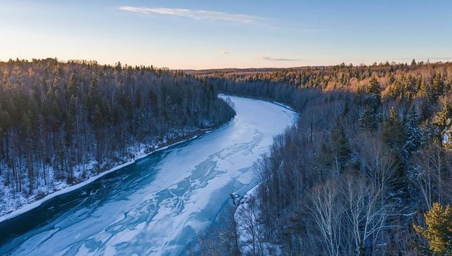 Winding frozen river cutting through snow-dusted forest at sunrise with fractured ice