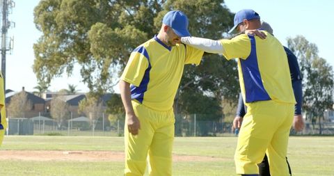Cricket players consoling teammate on suburban pitch wearing yellow and blue uniforms