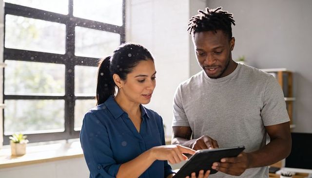 Two coworkers collaborating on tablet in bright modern office, teamwork and digital workflow