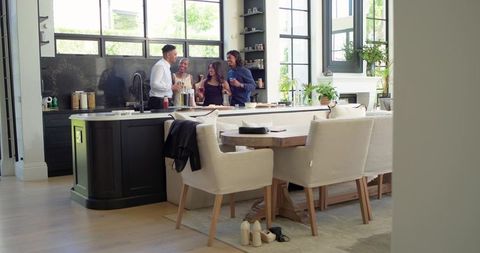 Friends chatting and toasting wine at modern open-plan kitchen island with natural light