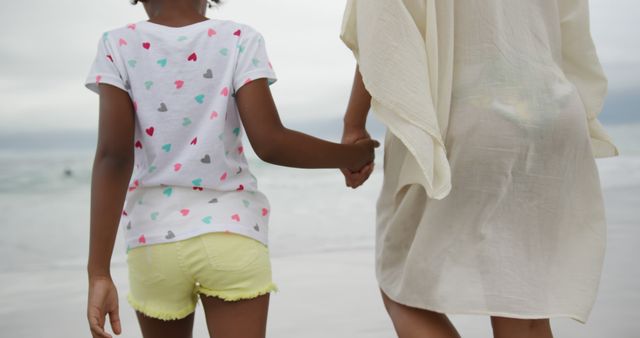 Midsection of african american mother and daughter holding hands on beach. Lifestyle, motherhood, childhood, summer, leisure and vacation.