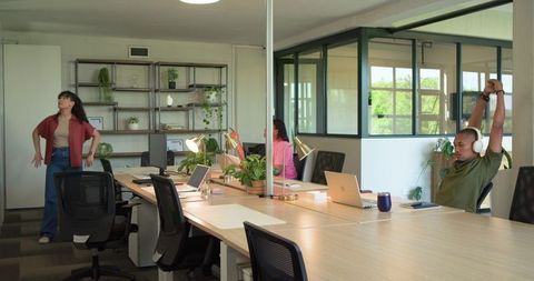 Diverse team stretching and collaborating in modern open-plan workspace with plants
