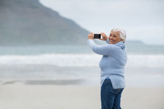 Portrait of senior woman photographing scenery using cell phone on the beach