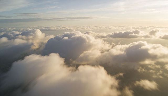 Gliding Sunlit Cumulus Clouds Over Faint Landscape at Golden Hour Aerial Serenity