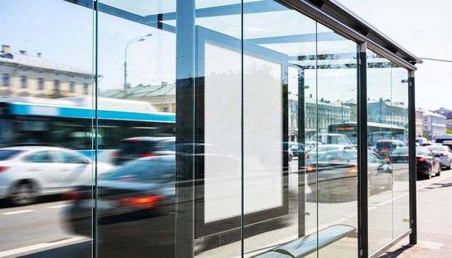 Urban glass bus shelter displaying blank ad panel on busy street with traffic reflections