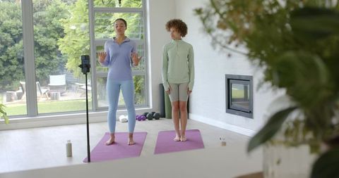 African american instructor leading home yoga class with student and smartphone recording
