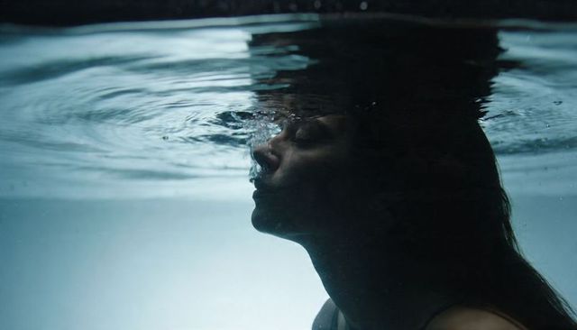 Underwater silhouette of woman exhaling bubbles at waterline, moody serene minimal profile
