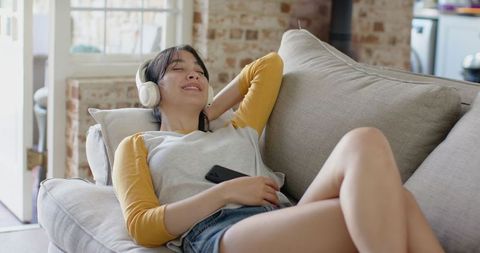 Asian woman relaxing on sofa with wireless headphones and smartphone