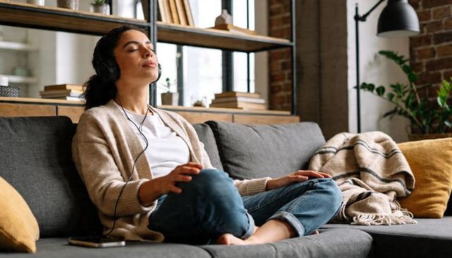 Woman relaxing on sofa listening to music with wired headphones in cozy loft