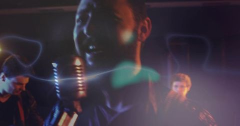 Lead Singer Singing Into Vintage Microphone on Moody Neon Stage with Guitarists and Haze