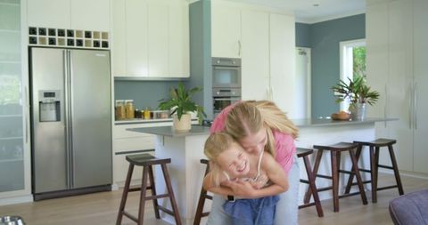 Mother hugging daughter laughing at bright modern kitchen island family moment warm lifestyle