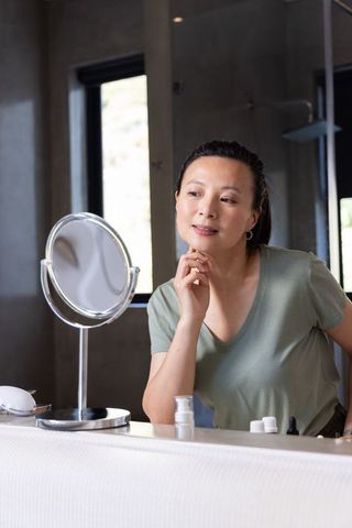 African american woman checking skin in mirror on bathroom vanity practicing morning skincare and se