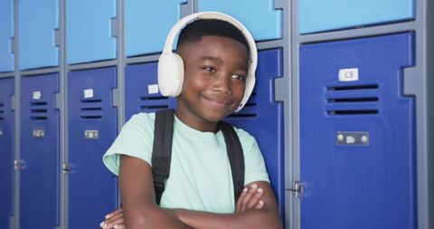 African american student leaning by blue lockers smiling while listening with white headset