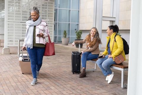 Senior woman following digital itinerary on smartphone while friends wait with luggage