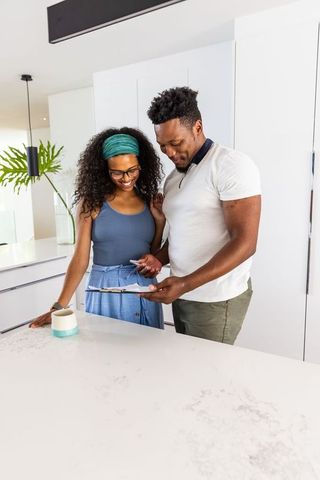 Black couple reviewing home paperwork at modern marble kitchen island with teal mug