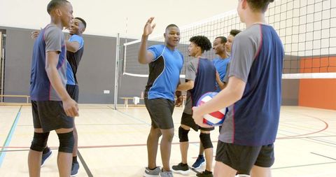 Multicultural male volleyball team celebrating victory on indoor court showing teamwork