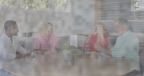 Four adults chatting at round wood table in bright modern kitchen during casual gathering