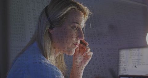 Woman adjusting headset and coding on laptop in moody home workspace with data overlay