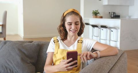 Young woman checking smartwatch while holding smartphone on minimalist sofa