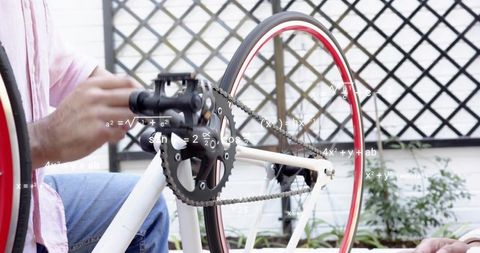 Man turning bicycle crankset with wooden rod on outdoor patio repair, couple collaboration