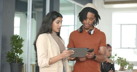 Collaborating on tablet and smartphone in modern open office with diverse professionals