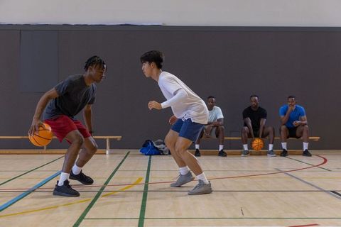 High-intensity one-on-one basketball drill between black and asian players in indoor gym