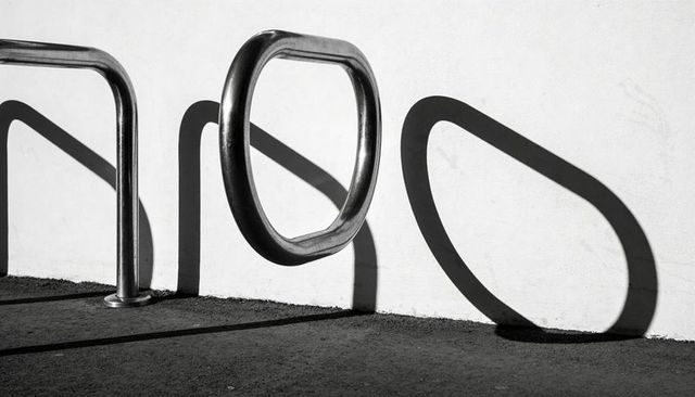 Polished bicycle racks casting long geometric shadows on white plaster wall, minimalist