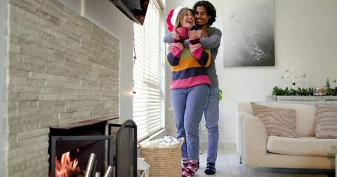 Couple embracing by cozy fireplace wearing santa hat and colorful striped sweater