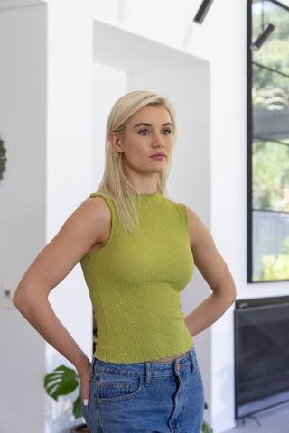 Young woman standing hands-on-hips in minimalist living room wearing lime-green top and jeans