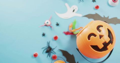 Halloween jack-o-lantern bucket featuring paper bats ghost cutouts and candy flatlay on blue
