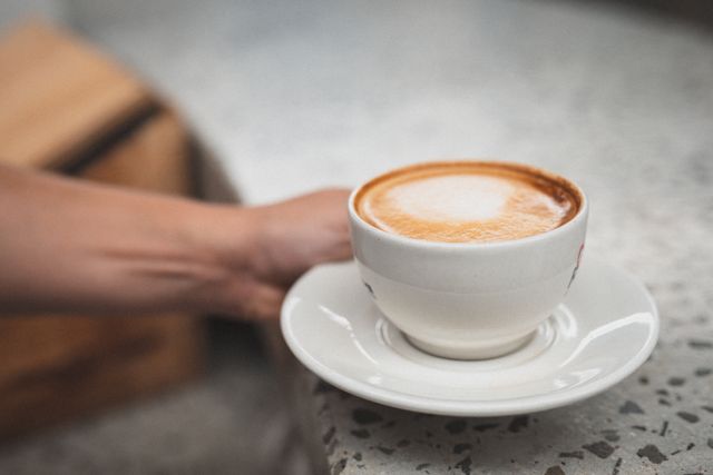 Close-up of a woman's hand placing a cup of coffee on a counter at a gym. Ideal for use in articles or advertisements related to fitness, leisure, coffee breaks, and relaxation. Can also be used to depict a moment of rest or enjoyment in a busy environment.