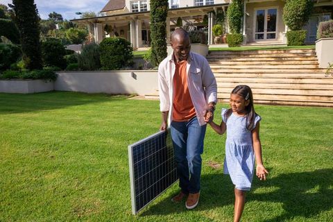 Father and Daughter Carrying Solar Panel in Sustainable Suburban Yard