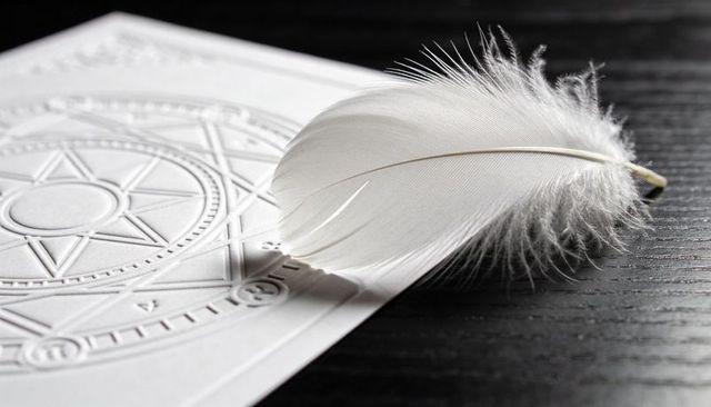Soft white feather casting shadow on embossed geometric star card on dark wood surface