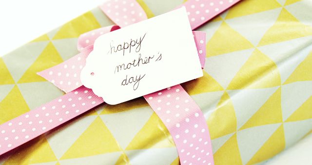 Brightly wrapped gift adorned with pink ribbon and 'Happy Mother's Day' handwritten tag. Suitable for advertising Mother's Day promotions, greeting cards, blog posts about Mother's Day gift ideas, and festive celebration themes.