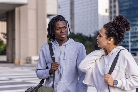 Urban commuters walking and talking across plaza carrying backpacks wearing hoodies