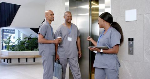 African american healthcare team talking near elevator with tablet in modern clinic lobby