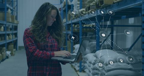Woman in Warehouse Using Laptop with Digital Icons Overlay