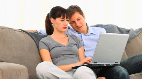 Couple Relaxing on Sofa with Laptop Browsing Together