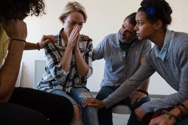 Friends consoling worried female while sitting on chair in art class