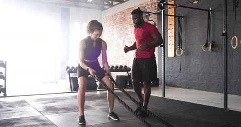 Trainer coaching client in battle rope fitness session at gym