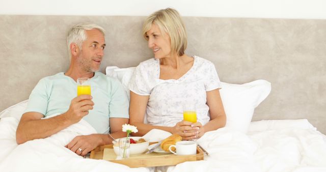 Older couple enjoying breakfast in bed together, showcasing love and relaxation. Ideal for use in advertisements targeting seniors, retirement living, healthy lifestyles, and romantic getaways. Suitable for brochures, greeting cards, or social media promoting products related to elderly well-being and comfort.