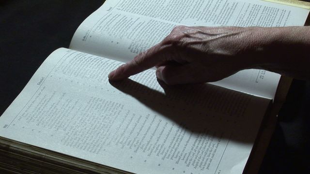 Hand points at Bible passage in illuminated text. Useful for illustrating religious study, faith concepts, academic research in theology. Excellent visual for presentations, blog posts or articles related to religious education, Christian faith, or scriptural references.