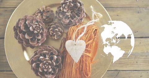 Rustic holiday flat-lay with pine cones, raffia bundle and wooden heart on gold plate with world map