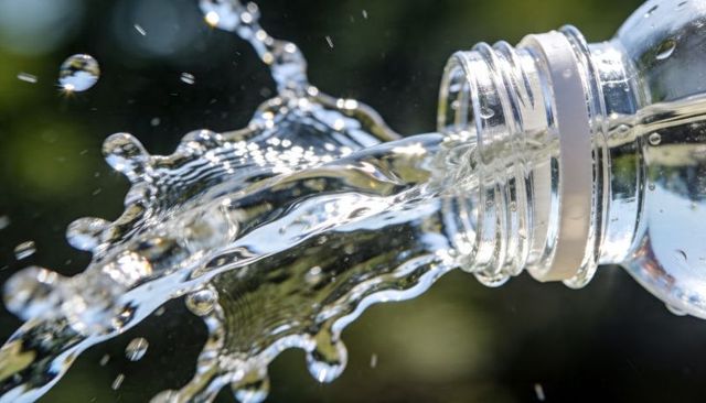 Pouring water from plastic bottle creating dynamic splash, droplets, sunlit reflections